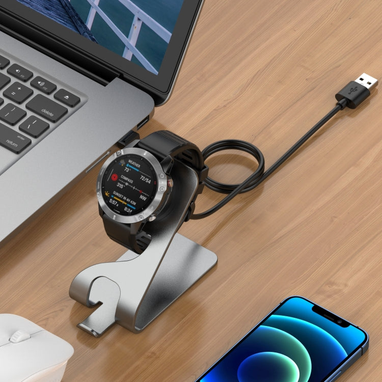 Metal smartwatch charger stand holding a smartwatch with connected USB charging cable.