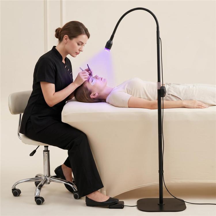 Black floor UV LED curing lamp with glowing bulb used beside seated client
