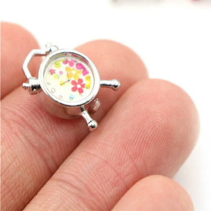 Mini alarm clock accessory with silver frame and floral face dial, handheld close-up