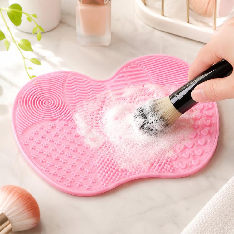 Pink silicone heart brush cleaning mat with textured scrubbing surface and makeup brush