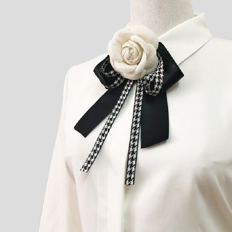 Rose bow brooch with black ribbons tied at the collar of a white top