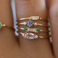 Gold-tone stacked ring with round blue center stone, green baguette accents, and pave bands
