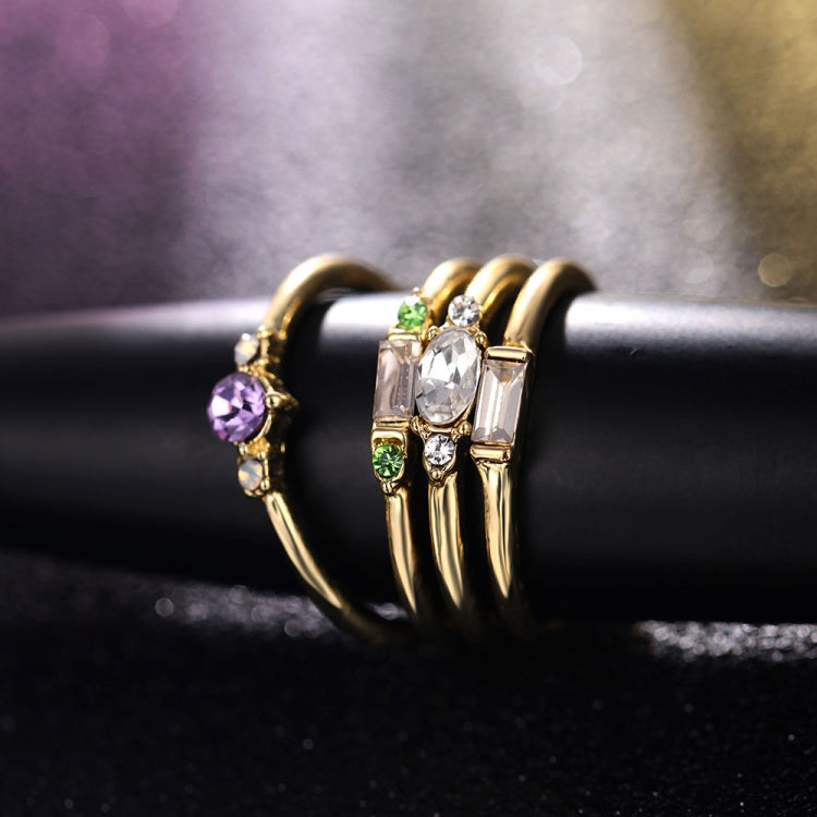 Gold-tone stacked rings with round purple, clear oval, and green baguette crystal settings