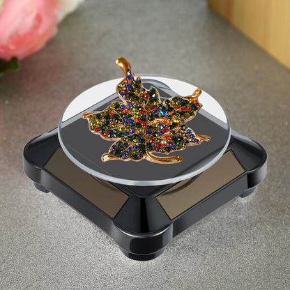 Black solar rotating display stand with glass top holding a jeweled leaf-shaped pin