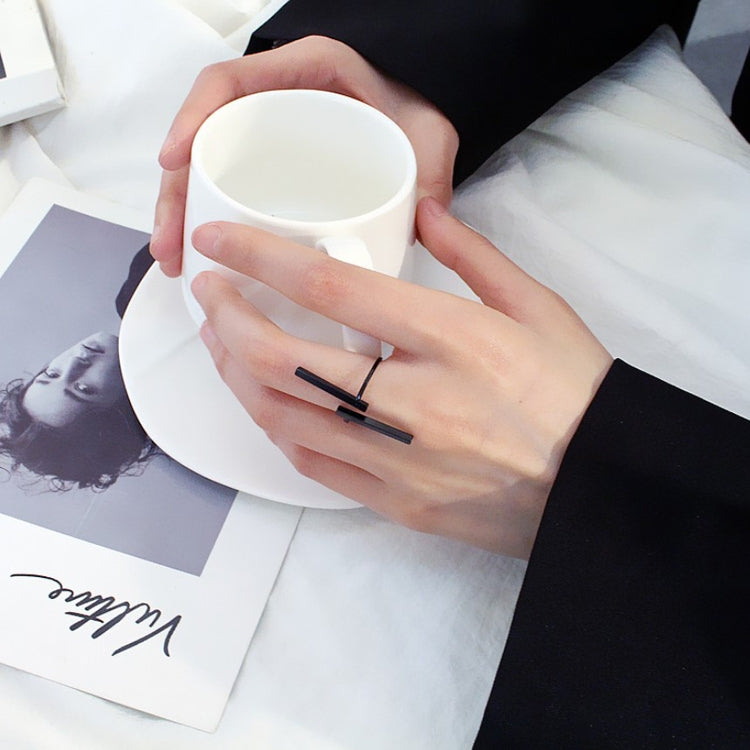 Black geometric open finger ring on hand near white mug, two bars on open band