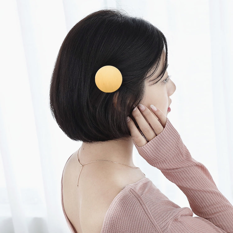 Round gold metal snap hair clip on dark hair, secured at the crown