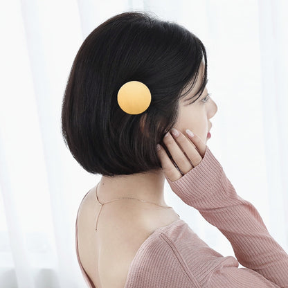 Round gold metal snap hair clip on dark hair, secured at the crown