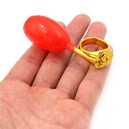 Red water-spray ring toy with gold lion-face ring and squeeze bulb on hand
