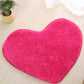 Bright pink heart-shaped bath mat with plush shag pile and non-slip edge binding.
