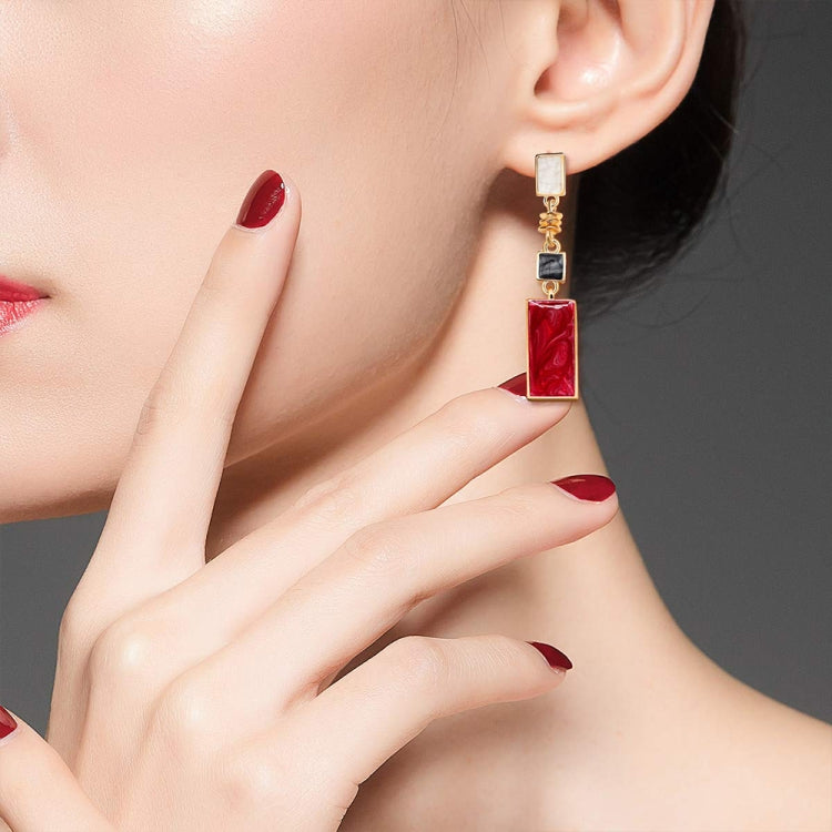 Worn red and black rectangular drop earrings with gold-tone hooks on model