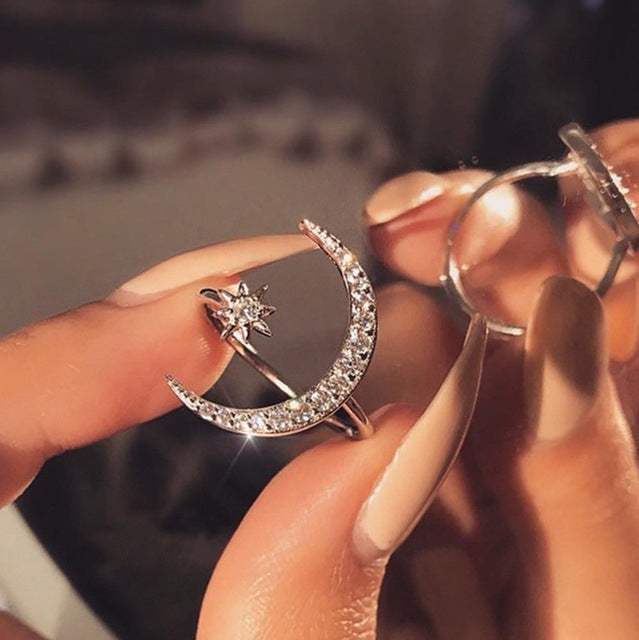 Silver-tone crescent moon crystal ring with star charm, close-up on finger