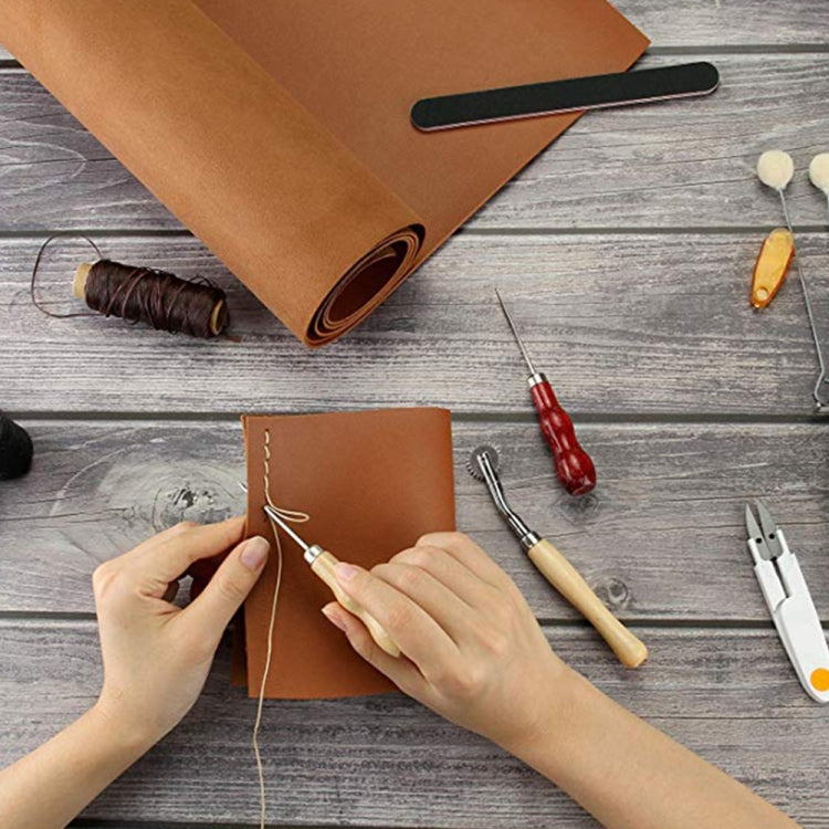 Leather craft kit in use with hands sewing a brown leather notebook cover