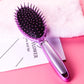 Purple oval hairbrush with black bristles, silver handle grip, air-cushion design.