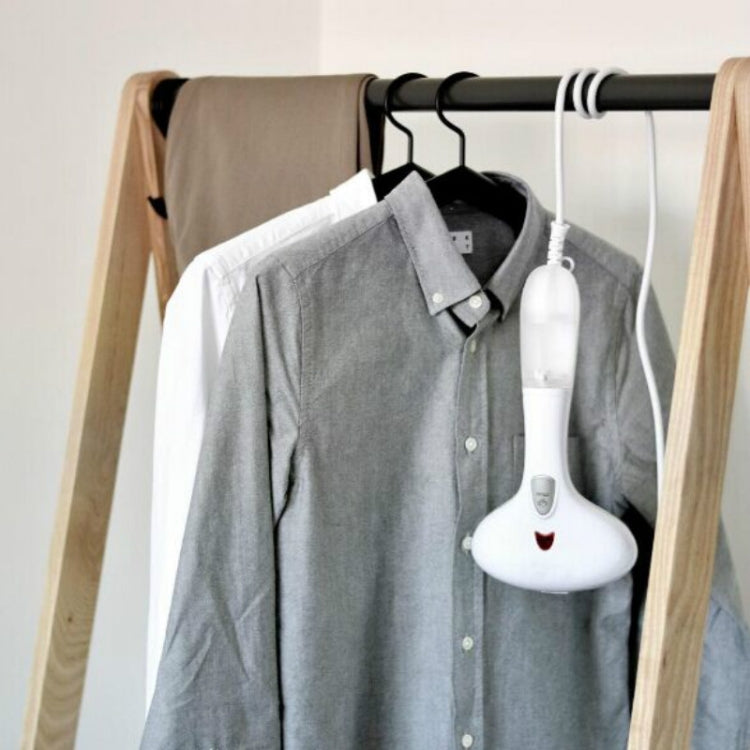 Handheld garment steamer steaming a hanging button-up shirt on a rack