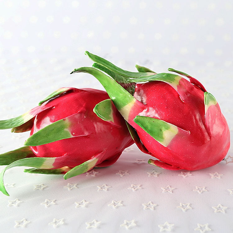 Pair of red dragon fruit ornaments with green leaves, resting on a star-patterned surface