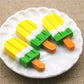 Yellow, green and orange striped ice cream stick resin cabochons on plate