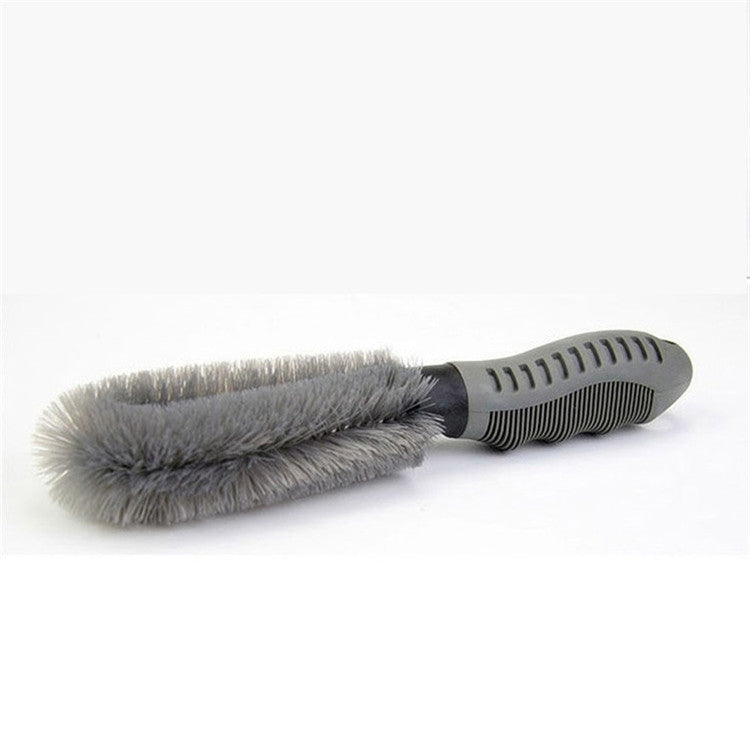 Car wheel cleaning brush lying flat, gray bristles on black ribbed handle