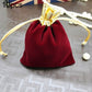 Red velvet drawstring jewelry pouch with gold bow and beige tie cords on surface