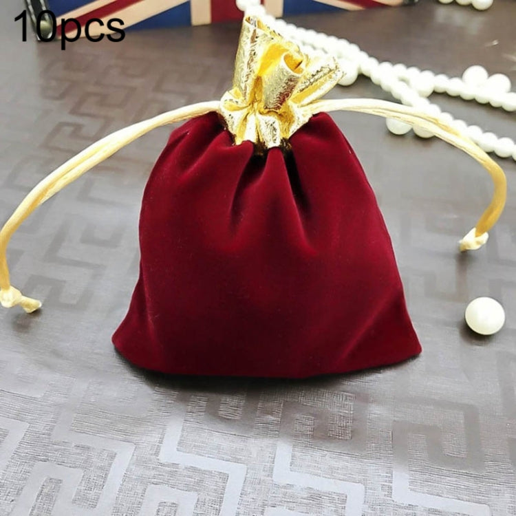 Red velvet drawstring jewelry pouch with gold bow and beige tie cords on surface