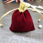 Red velvet drawstring jewelry pouch with gold bow and beige tie cords, pearl accents nearby