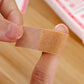 Waterproof adhesive medical bandage strip held on finger, tan porous pad and tape