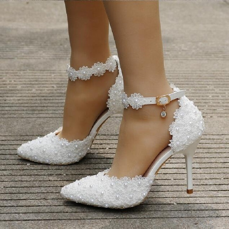 White lace ankle-strap heels on model feet with pointed toe and pearl-like bead detail