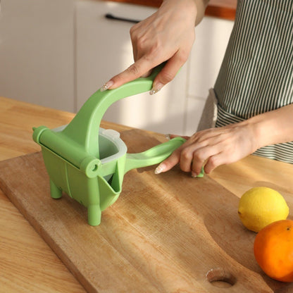 Green manual plastic hand juicer with scoop chute and spout, used on countertop