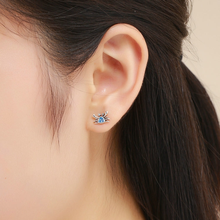 Oxidized silver crab earrings with blue heart-shaped gemstone worn on the ear
