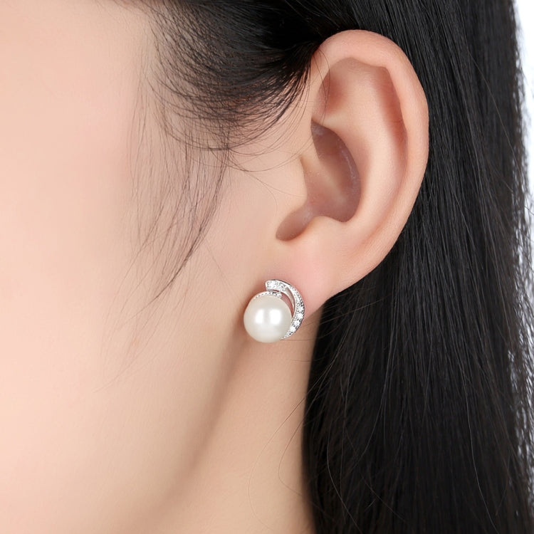White pearl stud earrings worn on ear with silver halo settings