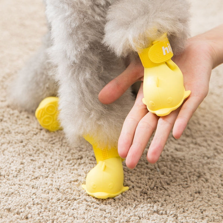 Yellow silicone pet rain boots set with cartoon paw bottoms; hand fitting boot on dog