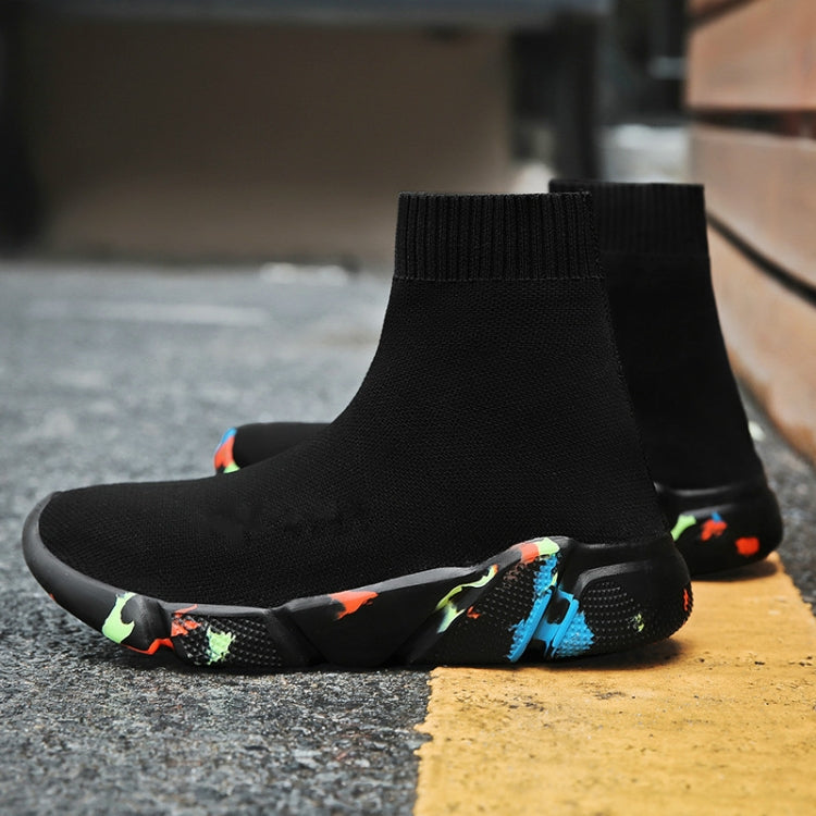Black knit sock sneaker boot with colorful speckled sole on textured pavement