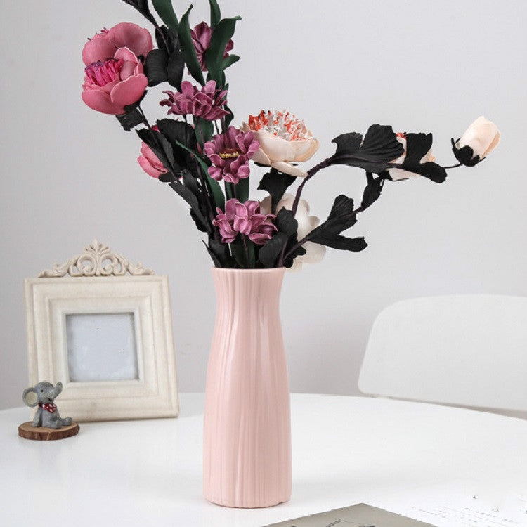 Pink ribbed plastic vase holding artificial flowers, tall desktop decoration