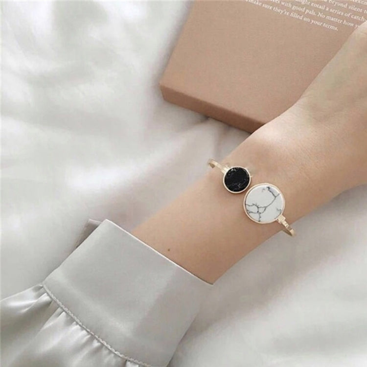 Gold-tone cuff bangle on wrist with black and white marble round centerpiece