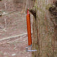 Orange tent stake mallet with claw head and red lanyard loop, against tree