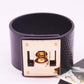 Wide black leather cuff bracelet with gold-tone square logo plate and metal clasp