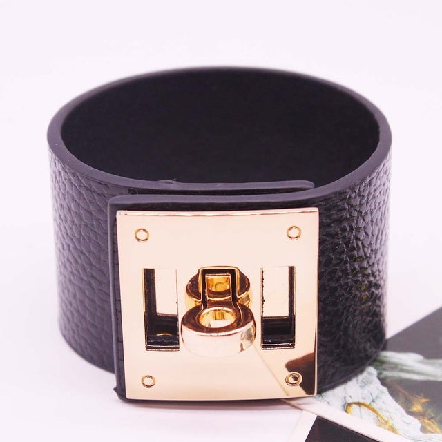 Wide black leather cuff bracelet with gold-tone square logo plate and metal clasp