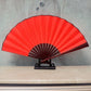 Red blank silk folding fan with dark red inner circle and maroon radial stripes on a stand.