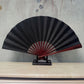 Black blank silk folding fan with maroon inner ribs, Chinese-style, on black stand