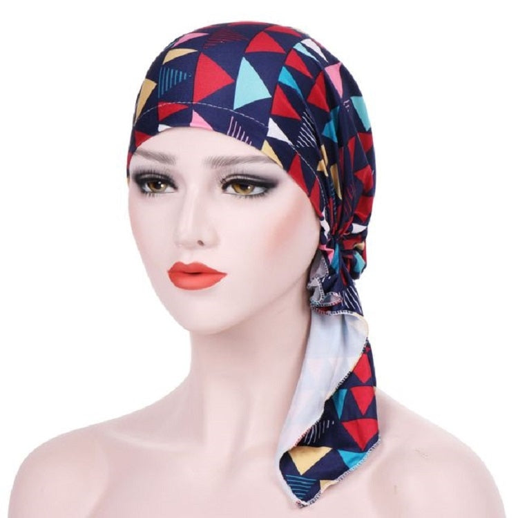 Stretch printed turban hat with long side tail, black base with red and teal geometric shapes