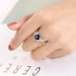 Silver-tone ring with blue oval crystal center and leaf-vine side stones