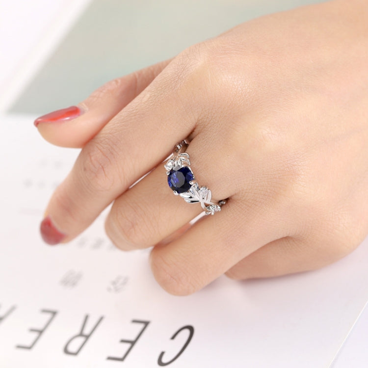 Silver-tone ring with blue oval crystal center and leaf-vine side stones
