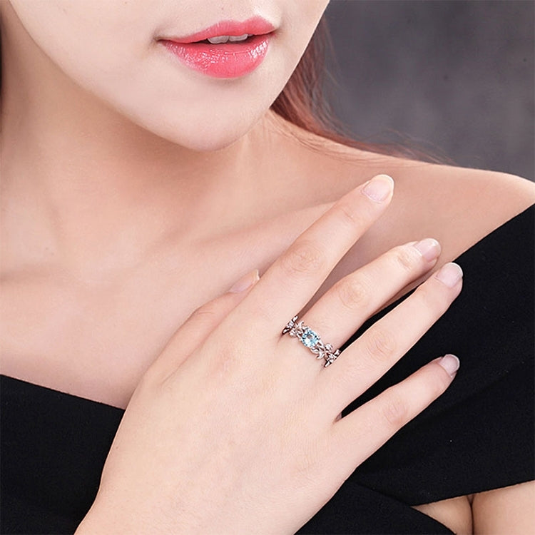 Silver-tone engagement ring with blue oval crystal center and vine leaf prongs