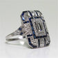 Square-cut crystal engagement ring with rectangular center stone and blue side accents