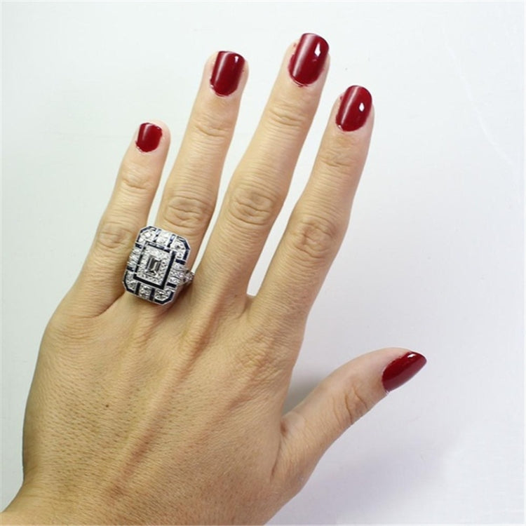 Square crystal ring on hand with rectangular center stone and blue gem accents