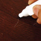 Hand using a white-capped furniture touch-up marker pen on dark wood surface