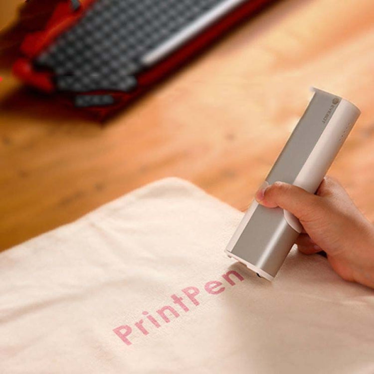 White inkjet pen mini printer held in hand on light fabric surface