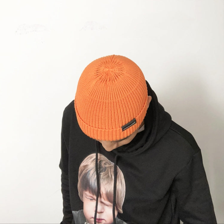 Orange short knit beanie on head with folded cuff and small logo tab
