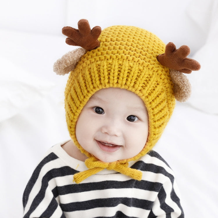 Baby wearing a yellow knitted hat with brown antler details and chin strap