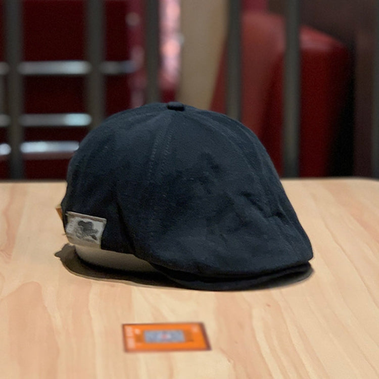 Black newsboy cap with curved brim and small metal logo patch on front