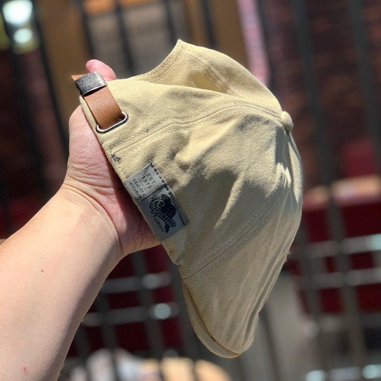 Cream canvas newsboy cap with tan leather strap and small fabric logo tag
